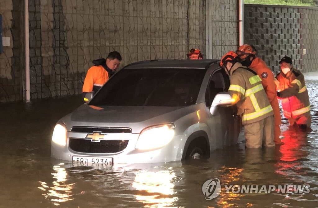 Firefighters help a driver on a flooded road in  in this photo provided by the Incheon Metropolitan Fire and Disaster Headquarters, as heavy rains pounded most of the country.