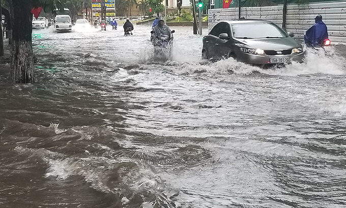 Cars and motorbikes struggle to go through a flooded street in Hai Phong City following heavy rains, July 2, 2020.