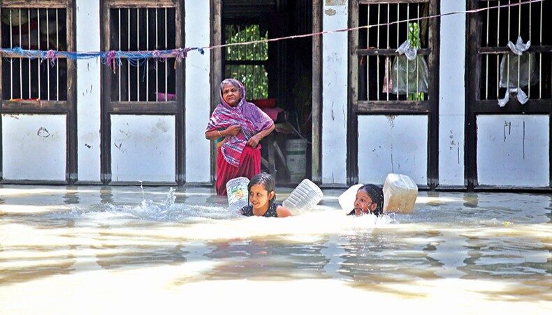 Two children swim to fetch fresh water as a woman looks on in a flood-hit area of Lauhajang upazila in Munshiganj on Tuesday.