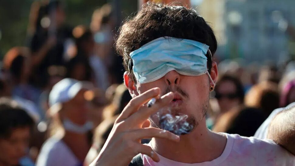 Click to enlarge man smokes a cigarette with his eyes covered by a face mask
