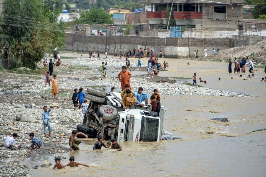 Youths sit on an overturned vehicle after flash floods triggered by heavy rainfalls affected the area in Jalalabad on August 26, 2020.