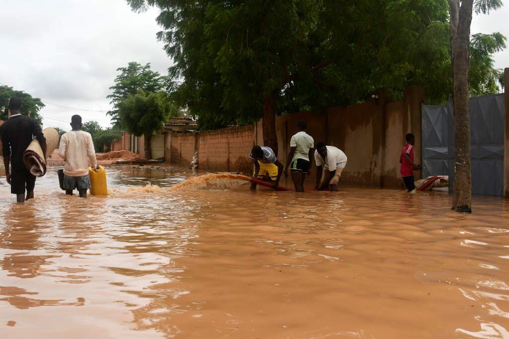 People carry their belongings while walking in a street flooded by the waters from the Niger river that flooded in the Kirkissoye neighbourhood in Niamey on August 27, 2020.