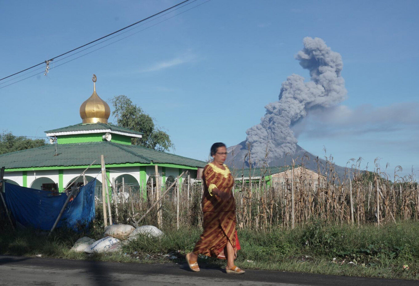 Click to enlarge A woman walks as Mount Sinabung spews