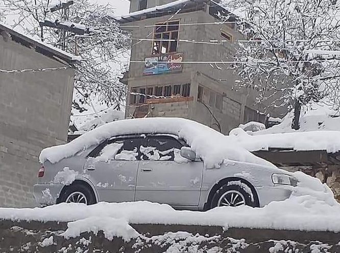 A car covered in snow appear stuck in what seems to be at least two feet of snow on a street in Lower Dir