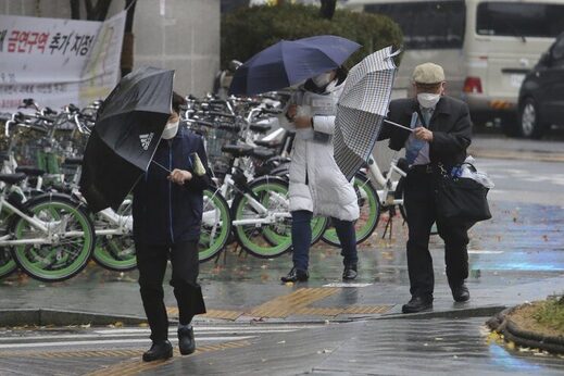 People wearing face masks try to manage their umbrellas in the rain in Seoul