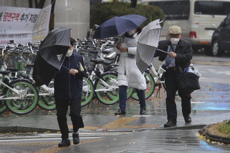 Click to enlarge People wearing face masks try to manage their umbrellas in the rain in Seoul
