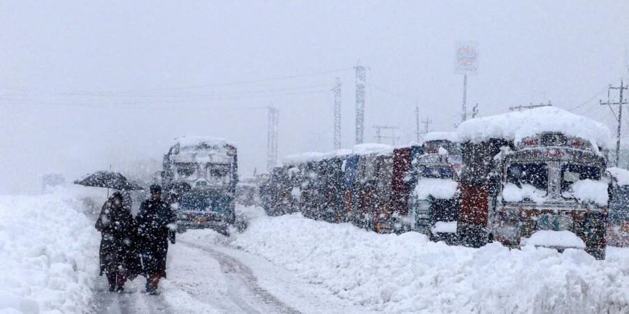 People walk past stranded vehicles on the Jammu-Srinagar National Highway during heavy snowfall, at Qazigund in Anantnag district of South Kashmir.
