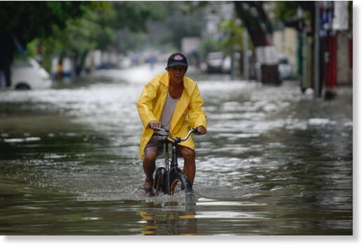 A man on a bicycle wades through a flooded