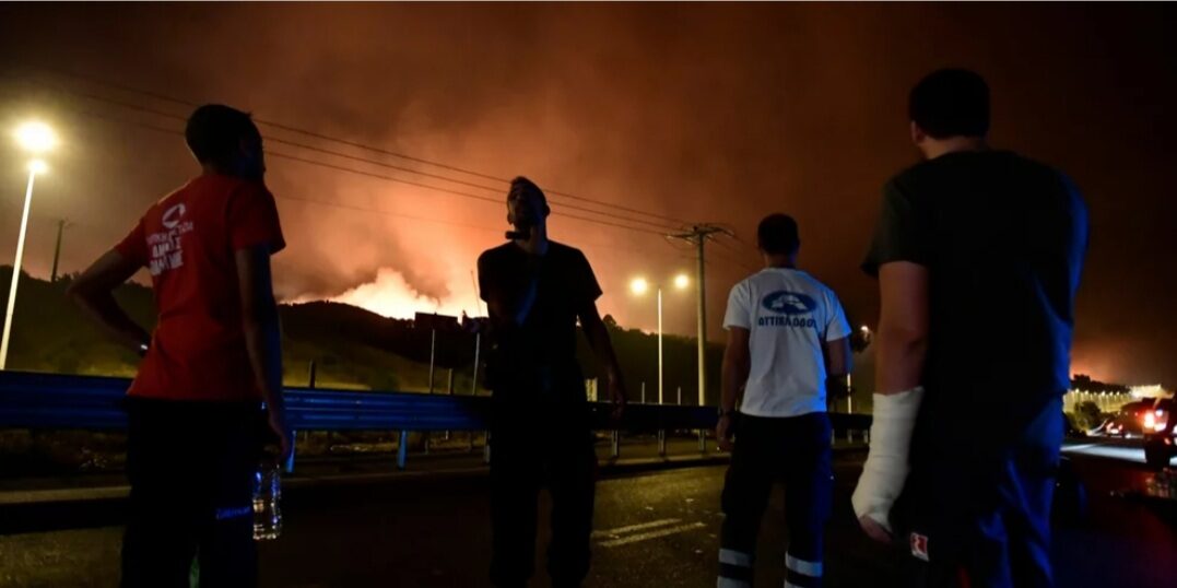 People watch the wildfire next to a highway in Afidnes area, northern Athens