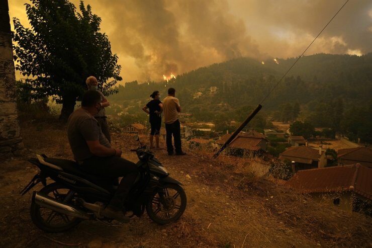 Local residents stand on a hill as flames approaching at Gouves village on the island of Evia, about 185 kilometers (115 miles) north of Athens, Greece, Aug. 8