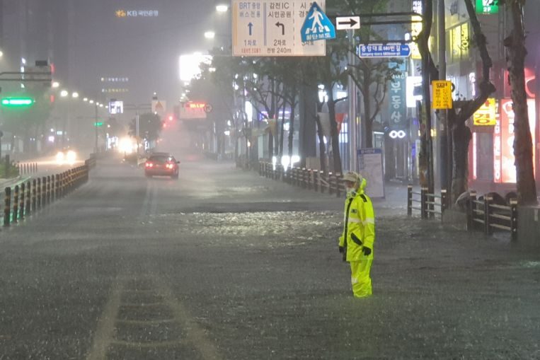 A police officer directs traffic on a submerged road in the port city of Busan, on Aug 24, 2021.