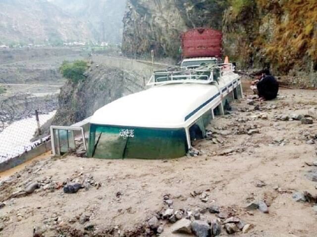 Men sit beside a coach buried under a landslide on KKH in Khushi area of Upper Kohistan on Wednesday.