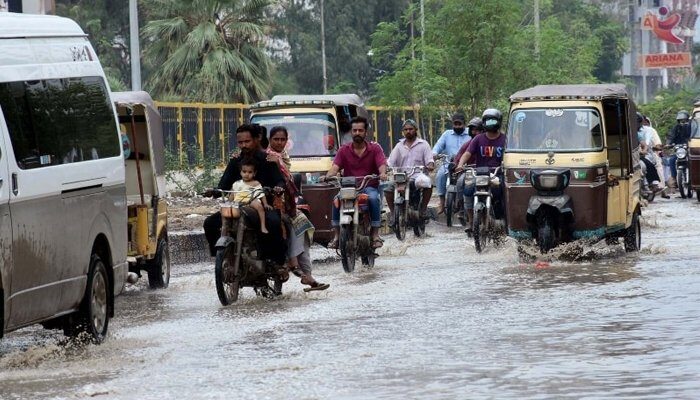 Commuters wade through rainwater after heavy rainfall in Karachi on Saturday