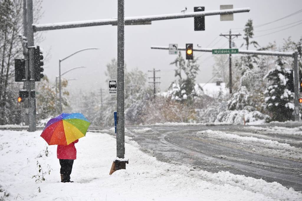 Click to enlarge A woman waits at a bus stop on East 36th Avenue as snow falls on September 24, 2021.
