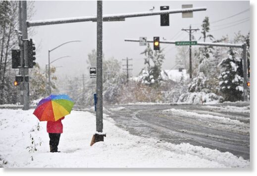 A woman waits at a bus stop on East 36th Avenue as snow falls on September 24, 2021.