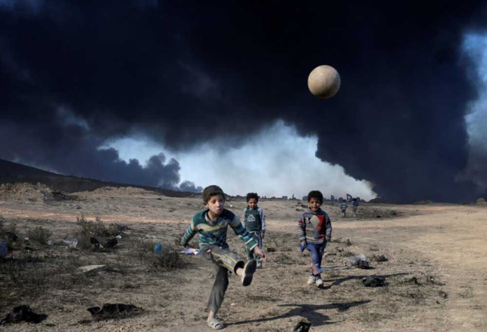 Boys play in front of burning oilfields in Qayyara, south of Mosul, Iraq, 2016.