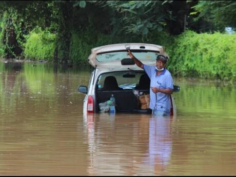 Peter Dawson, a taxi operator, is trapped in floodwaters on Orange Street in Montego Bay after heavy rainfall on Monday. Firefighters subsequently assisted him in removing his vehicle.