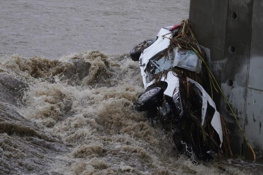 Click to enlarge A vehicle is wedged against a bridge pillar in the surging Los Angeles River on Tuesday.