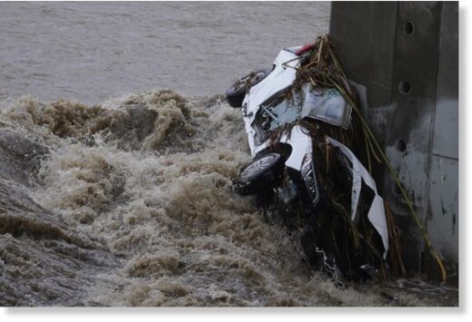 A vehicle is wedged against a bridge pillar in the surging Los Angeles River on Tuesday.