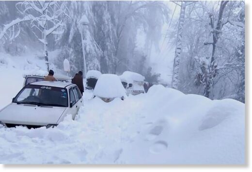 People walk past vehicles trapped in heavy snow in Murree