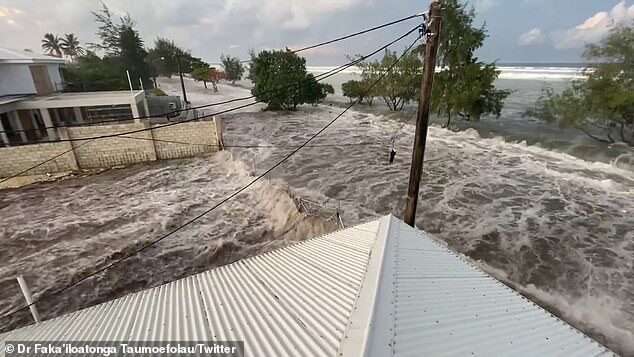 Click to enlarge A tsunami has struck Tonga sending terrified locals fleeing for high ground as huge waves crashed over roads and into homes (pictured, tsunami waves begin to overwhelm coastal homes in Tonga on Saturday)