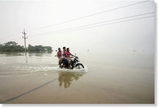 People ride on a bike on a submerged road during a widespread flood in Sylhet
