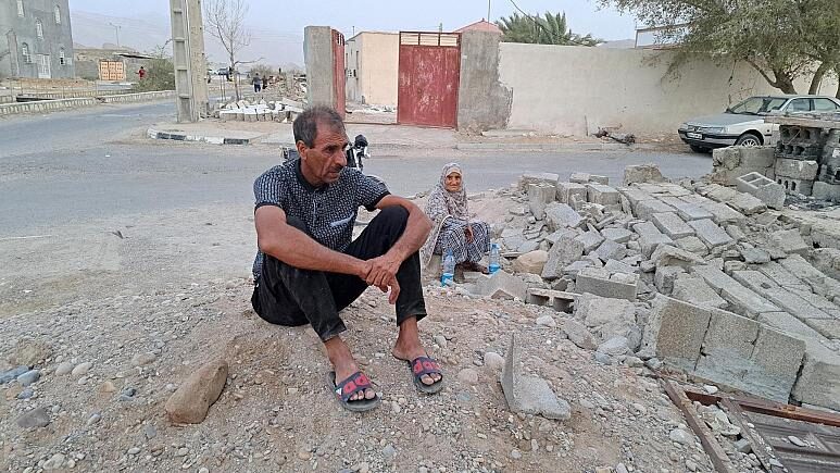 Click to enlarge People sit by the rubble amidst destruction in the aftermath of a 6.0 magnitude earthquake in Iran's southern Hormozgan province on 2 July.