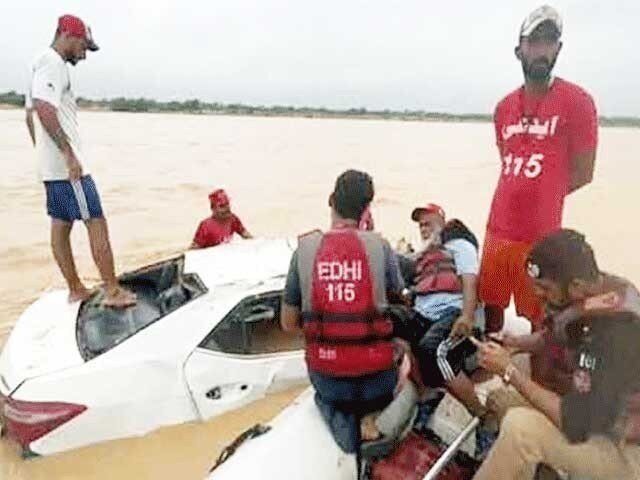 Click to enlarge Edhi rescue officials pictured while recovering a damaged vehicle that got swept away in a flash flood near Kathore in Karachi.