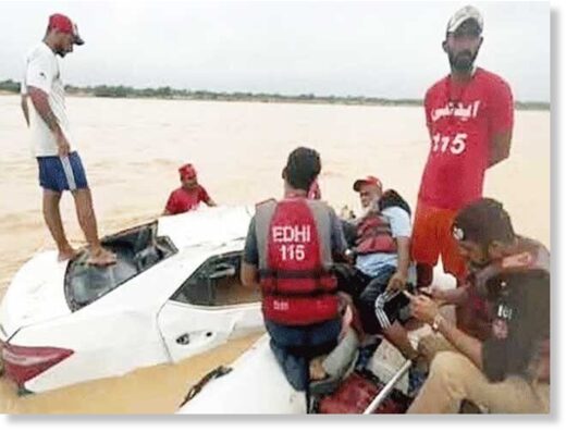 Edhi rescue officials pictured while recovering a damaged vehicle that got swept away in a flash flood near Kathore in Karachi.