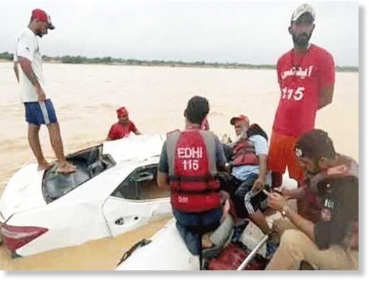 Click to enlarge Edhi rescue officials pictured while recovering a damaged vehicle that got swept away in a flash flood near Kathore in Karachi.