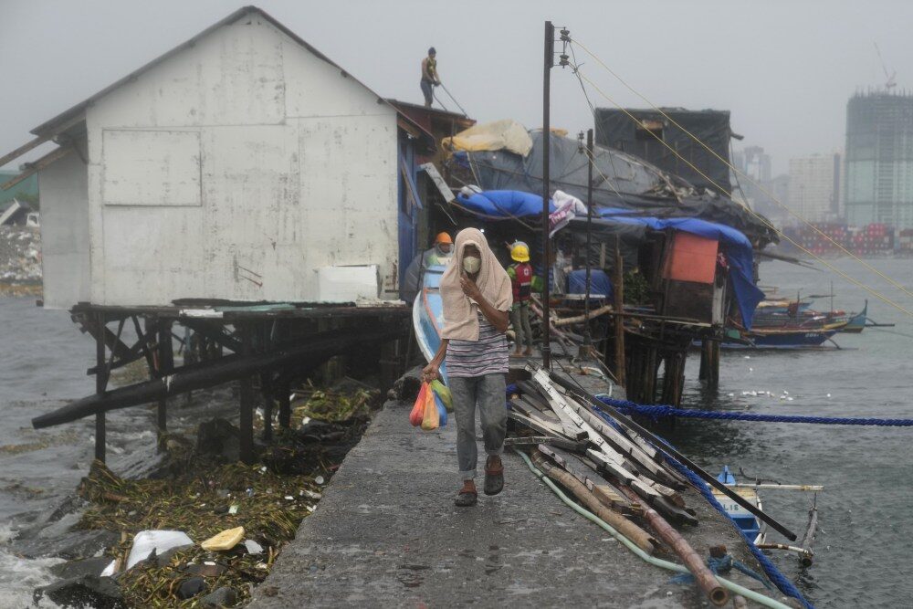 Click to enlarge A man carries bags of food while another reinforces their roof as they prepare for the coming of Typhoon Noru in the Philippines capital Manila on Sunday.