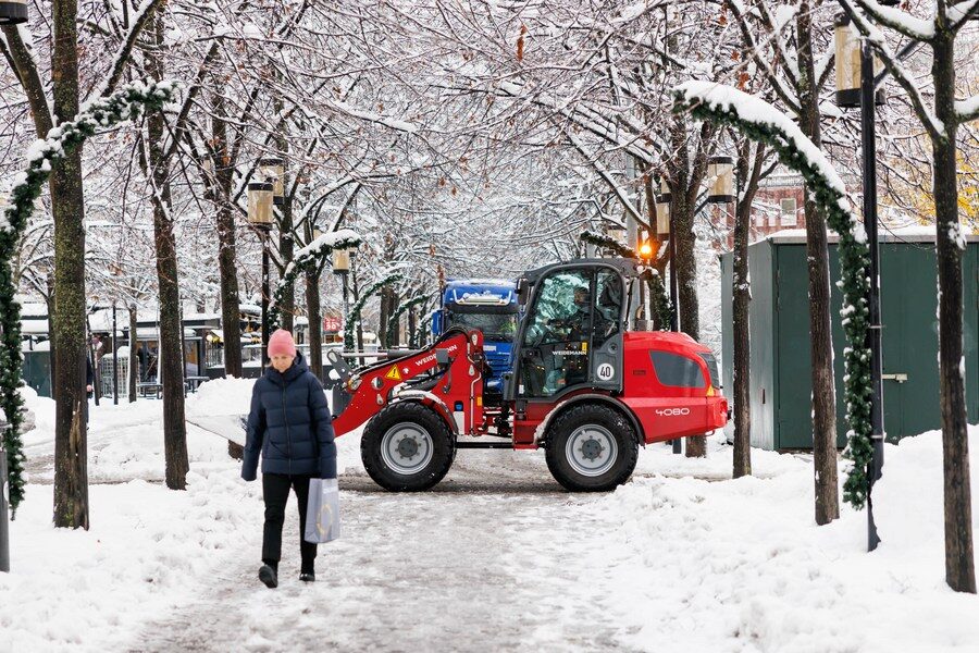 Click to enlarge woman walks on a snowy road as a snowplow clears the road in Stockholm, Sweden on Nov. 21, 2022.