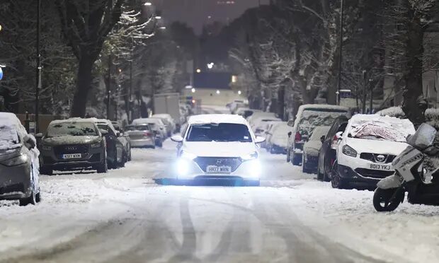 A car drives along a snow-covered road in the early morning at Willesden Green, north-west London.