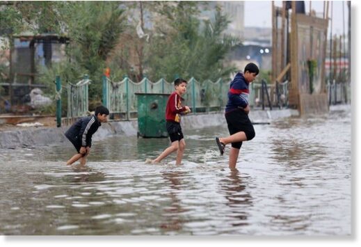 Iraqi children cross a flooded street in the Iraqi