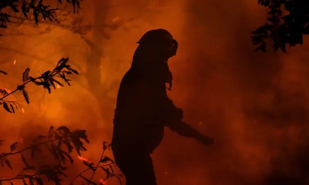 A firefighter works as a wildfire burns parts of