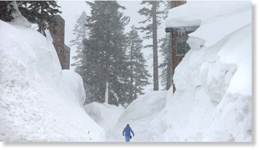 A person walks near snowbanks obscuring condominiums as snow falls in the Sierra Nevada mountains from yet another storm system which is predicted to bring heavy snow to higher elevations on March 28, 2023, in Mammoth Lakes, Calif