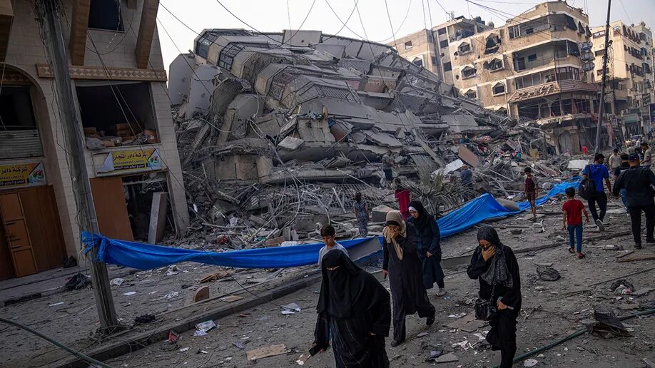 Palestinians walk by the rubble of a building after it was struck by an Israeli airstrike, in Gaza City