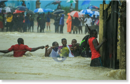 Click to enlarge A woman is assisted to safer ground after heavy