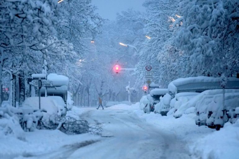 A man crosses a road early in the morning after heavy snowfall in Munich