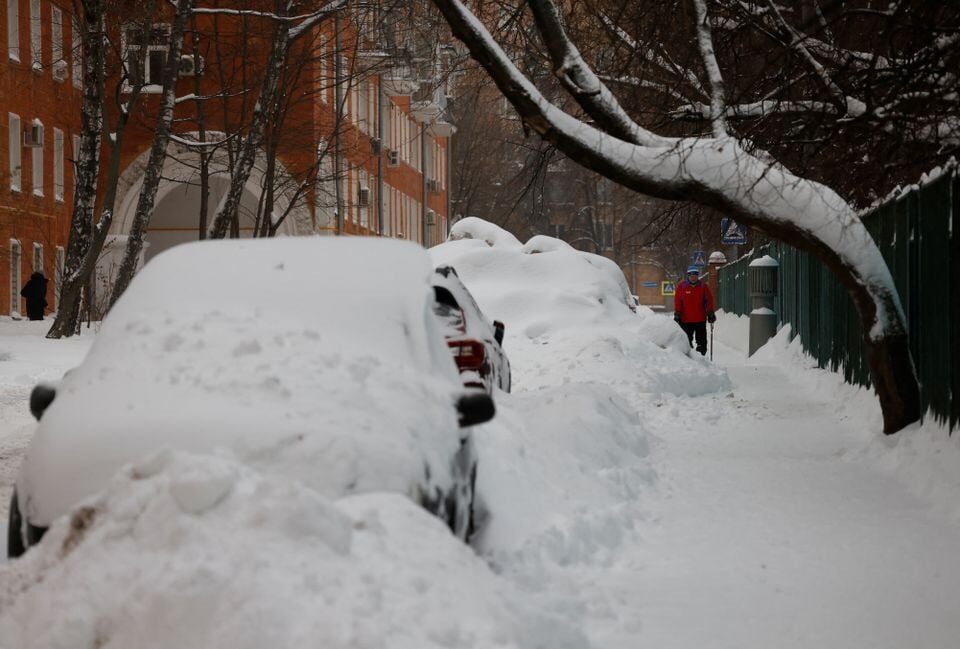 A man walks past cars covered with snow after