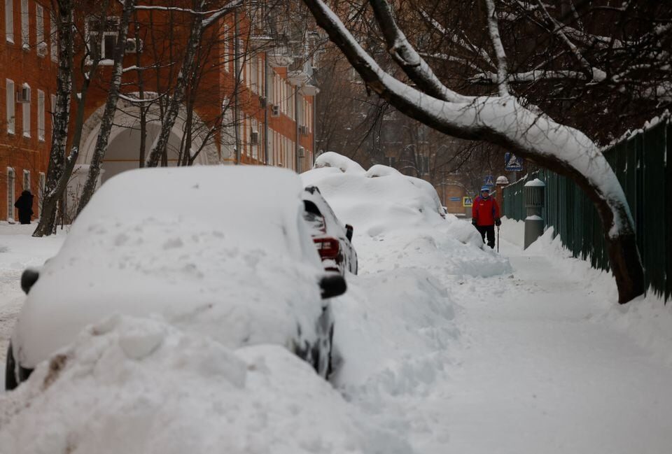 Click to enlarge A man walks past cars covered with snow after