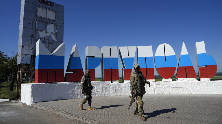 FILE PHOTO: Russian soldiers walk past a repainted sign outside Mariupol, Russia, June 12, 2022