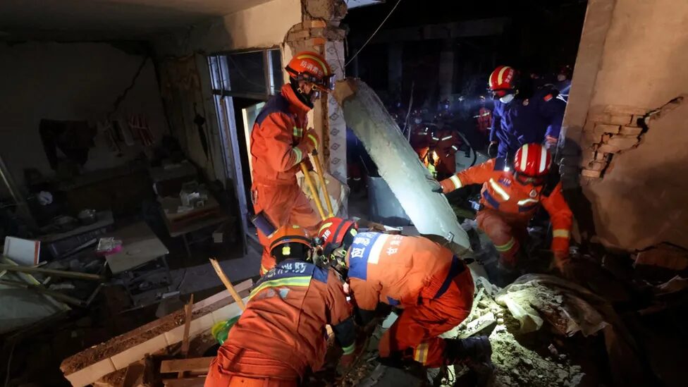 Click to enlarge Rescuers in orange outfits climb through damaged buildings in Kangdiao village in Jishishan county