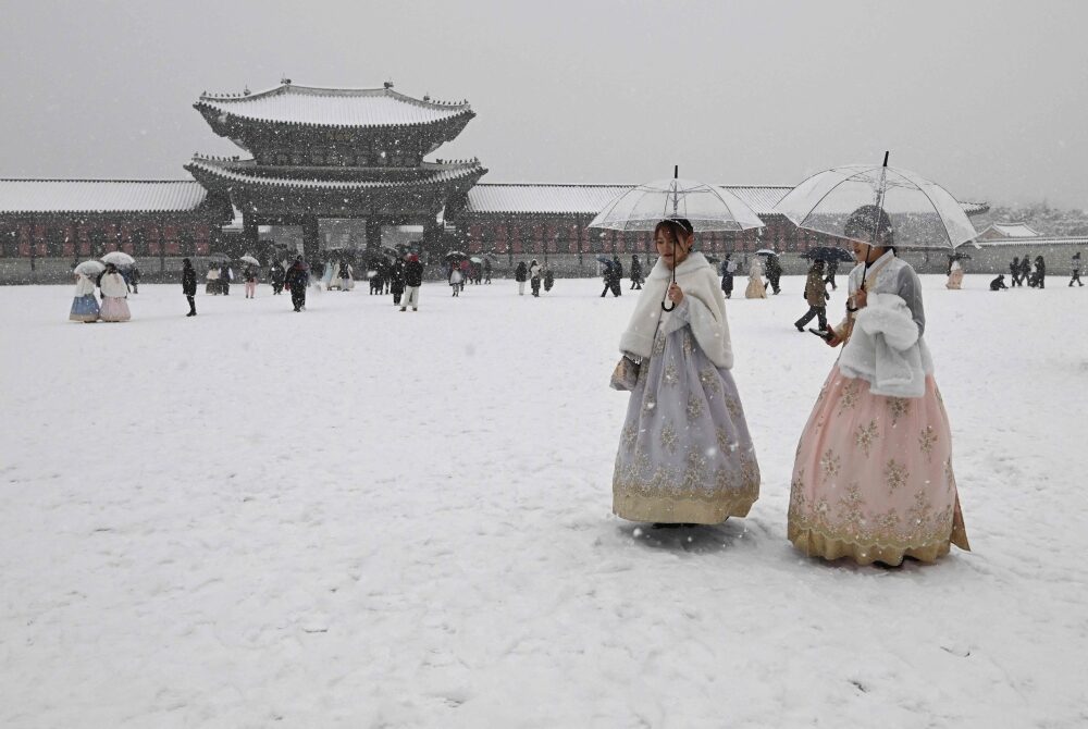Visitors wearing traditional hanbok dress walk in the snow at Gyeongbokgung palace in central Seoul on December 30, 2023.