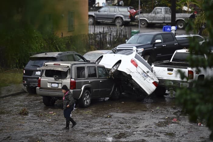 A woman walks by cars damaged by floods during a rainstorm in San Diego on Monday