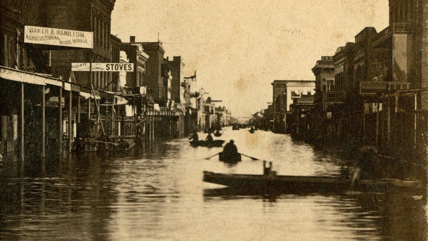 Click to enlarge Shows buildings including Baker & Hamilton, Gilday; flooded streets with men in rowboats.