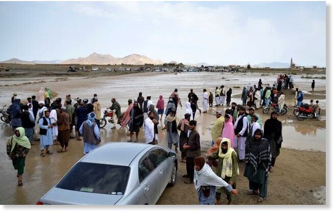 People wait to cross a flooded area in the Spin Boldak district of Kandahar province