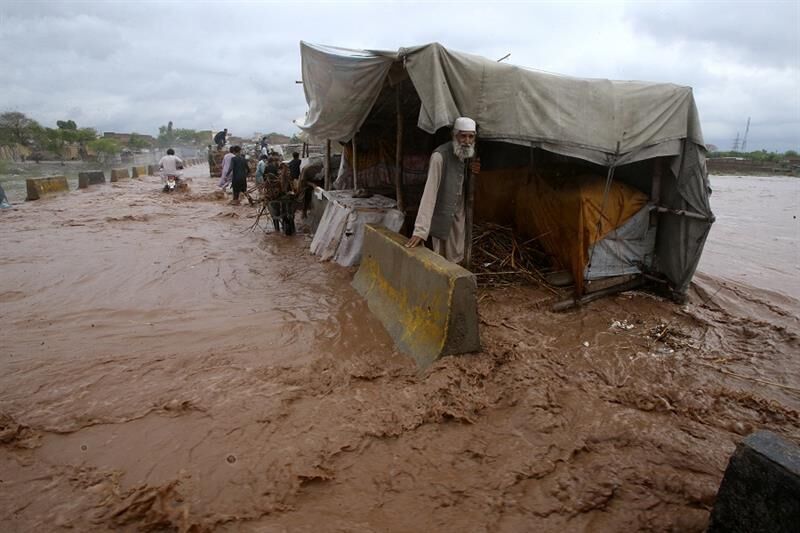 People stand beside a makeshift stall set up on the bank of a stream, which is overflowing following heavy rains, on the outskirts of Peshawar, Pakistan, April 2024.