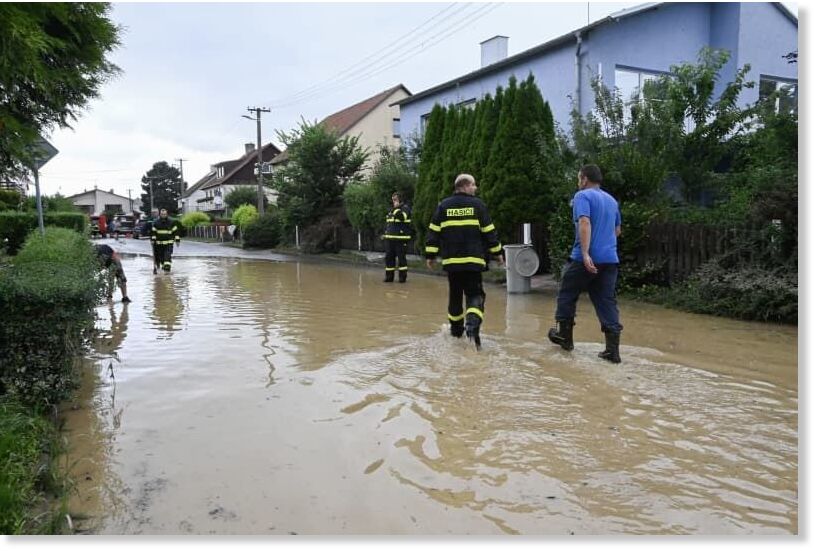 Click to enlarge Members of the Czech emergency services walk through a flooded street following heavy rains in the Czech Republic's east.