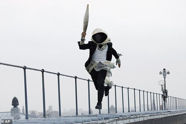 Click to enlarge A masked torch bearer runs atop the Musee d'Orsay, in Paris, France, during the opening ceremony